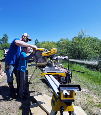 Lukas Gotto works with second grader Archer Swaggert with a large saw during the recent construction of a bridge/boardwalk behind Discovery Middle School in Alexandria this past summer.