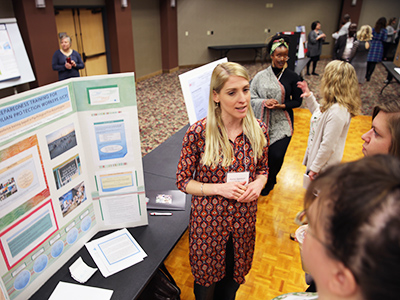 This is a photo of Karen Spencer explaining her research during the poster session at the 16th annual Doctoral Research Symposium held on March 7 on the Twin Cities Campus.